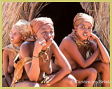ǂKhomani-San women with traditional clothing and decoration, resting outside the entrance to one of their temporary thatched shelters in South Africa’s ǂKhomani-San Cultural Landscape UNESCO world heritage site